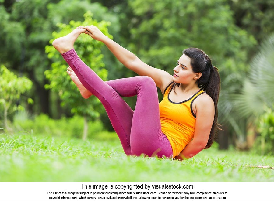 Indian Young Woman Doing Yoga Practice Hand Holding Feet In-Park