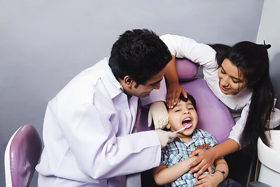 Indian dentist examining Kids teeth with mother watching dental clinic