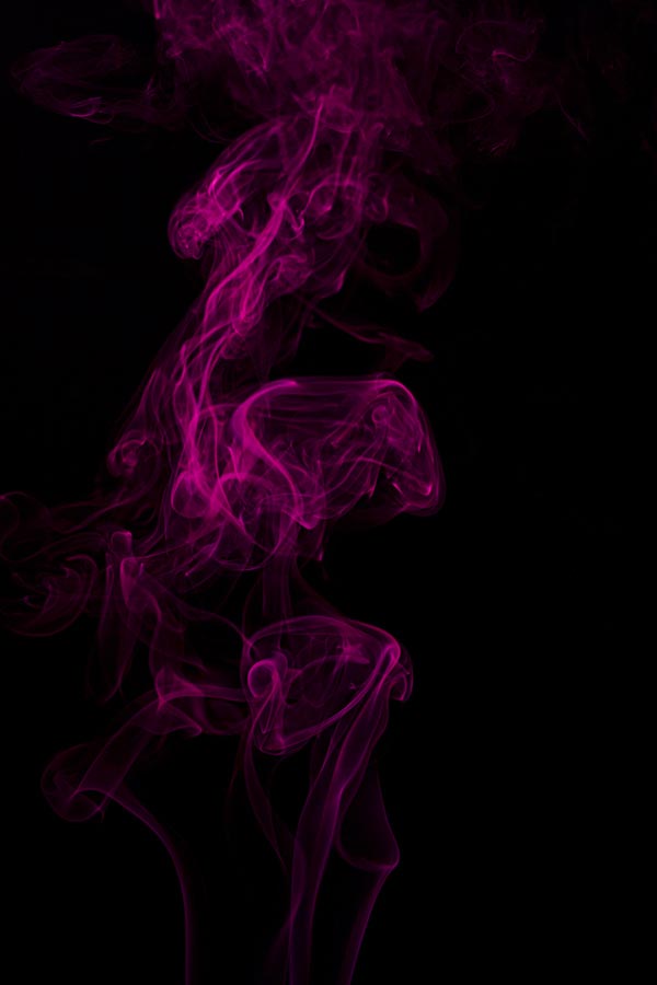 Pink smoke coming-up from an-incense stick over a black background