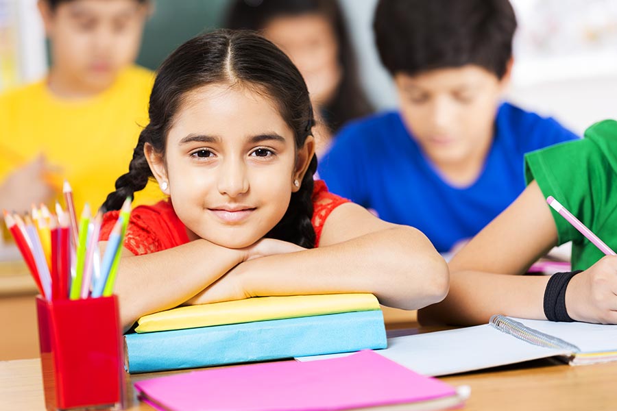 Primary School LittleGirl Student Sitting AtDesk With Students