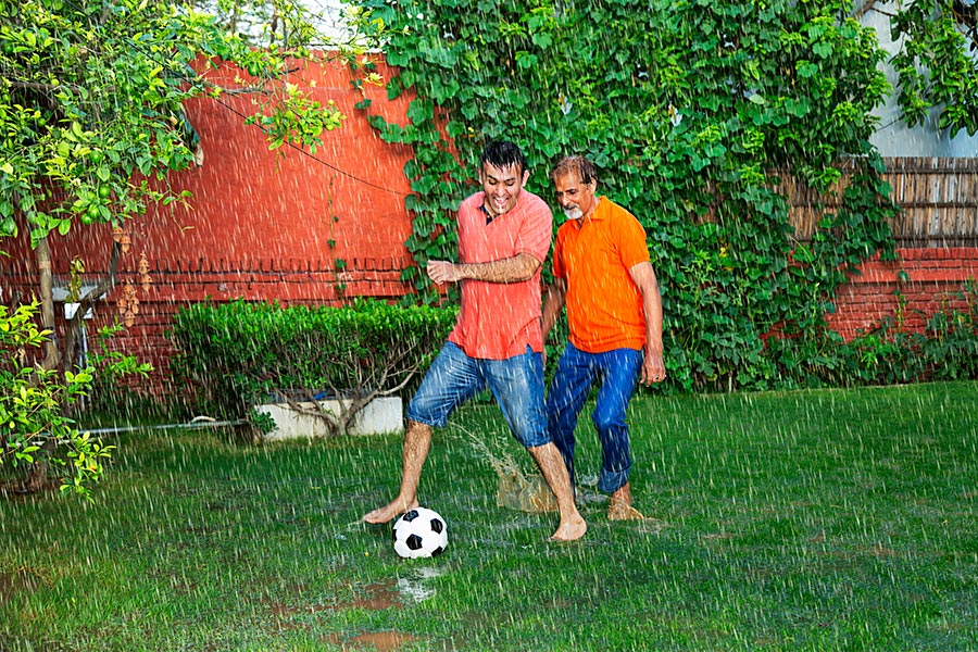 Father and Adultson playing football Soccer inthe Rain ingarden Home