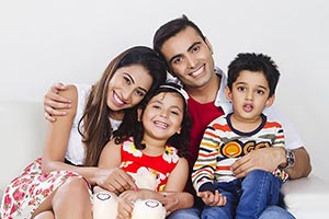 Parents Kids Sitting Sofa At Home Smiling